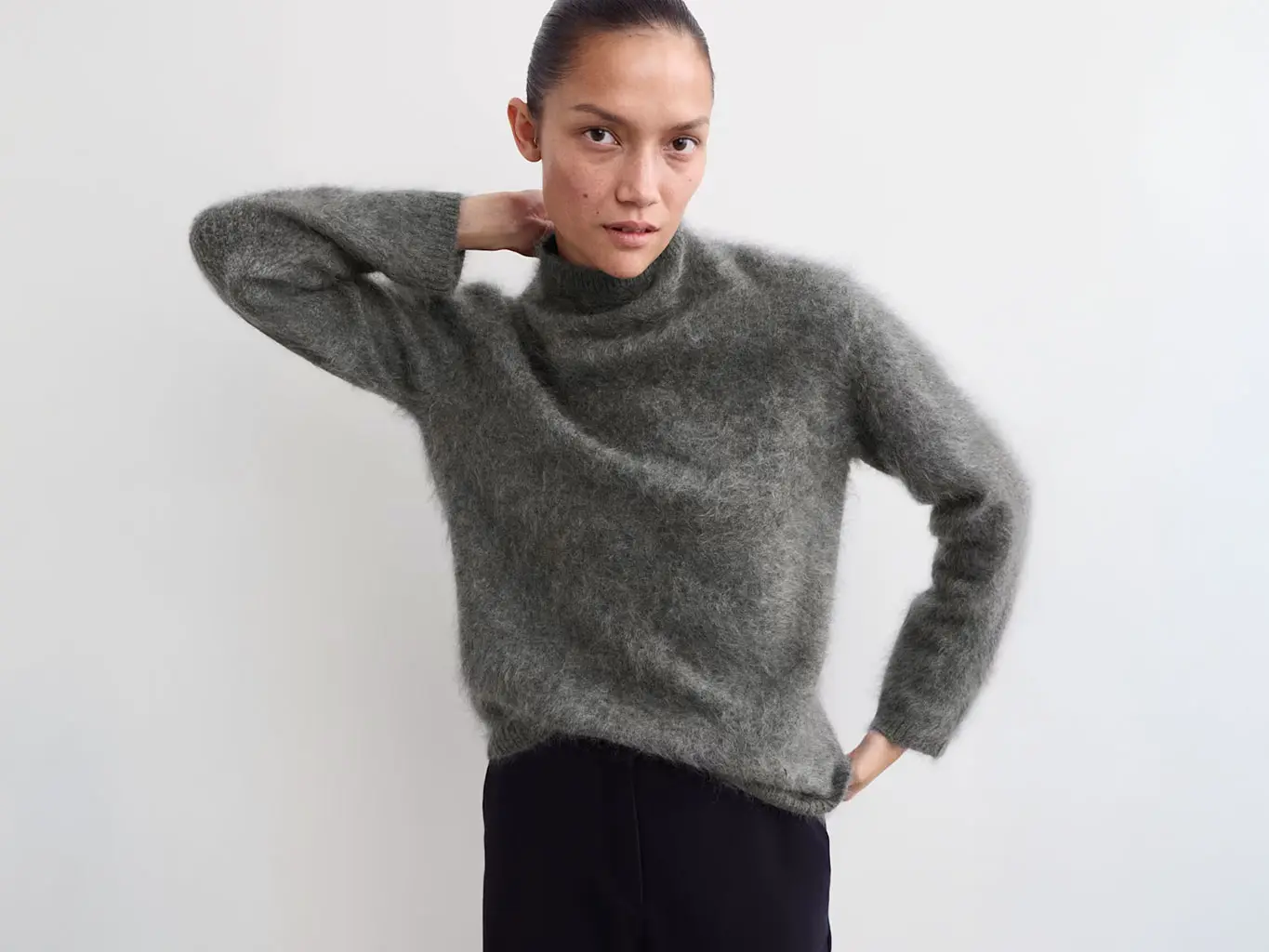 Woman wearing grey funnel-neck jumper with black trousers