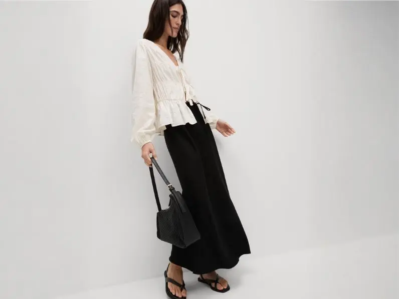 A woman wears a long skirt outfit featuring a white blouse, black maxi skirt and handbag
