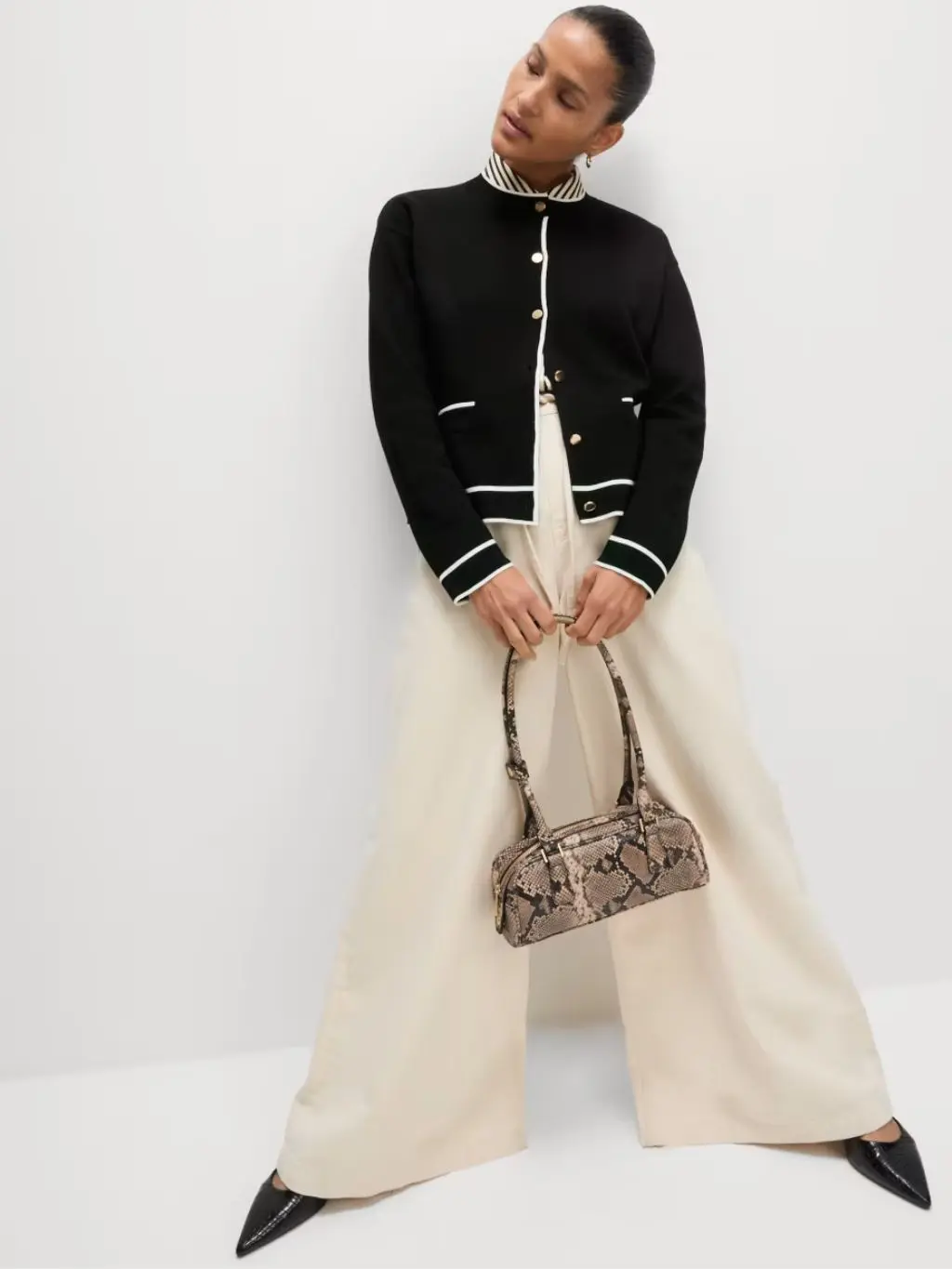 A woman wears white wide leg trousers, a knitted jacket and striped shirt