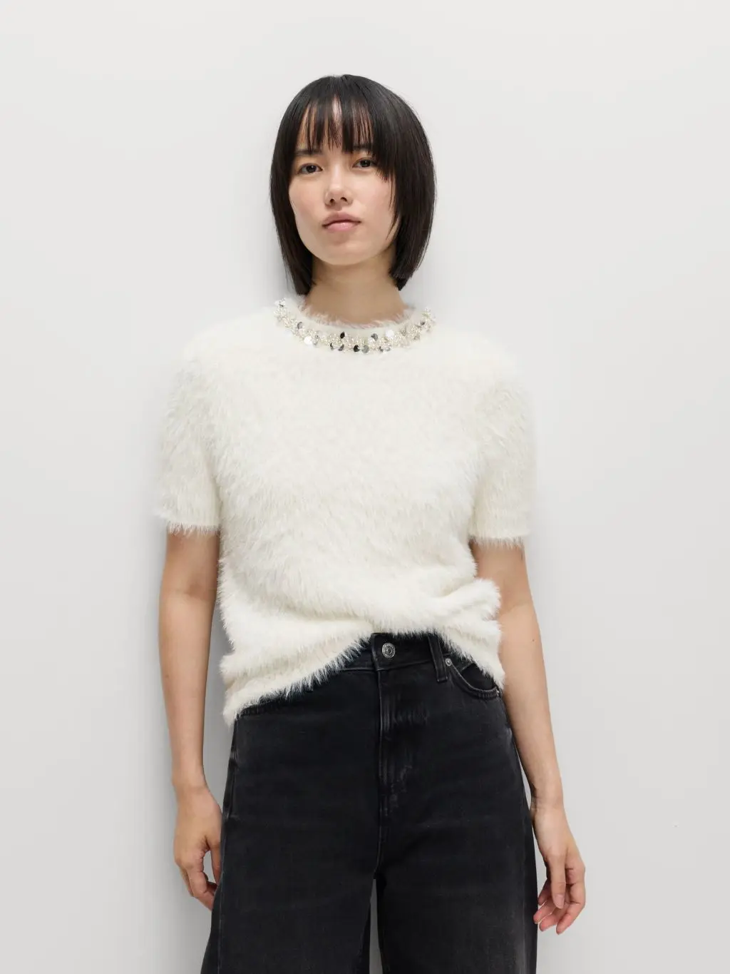 A woman wears a short sleeved fluffy knit with an embellished crew neck