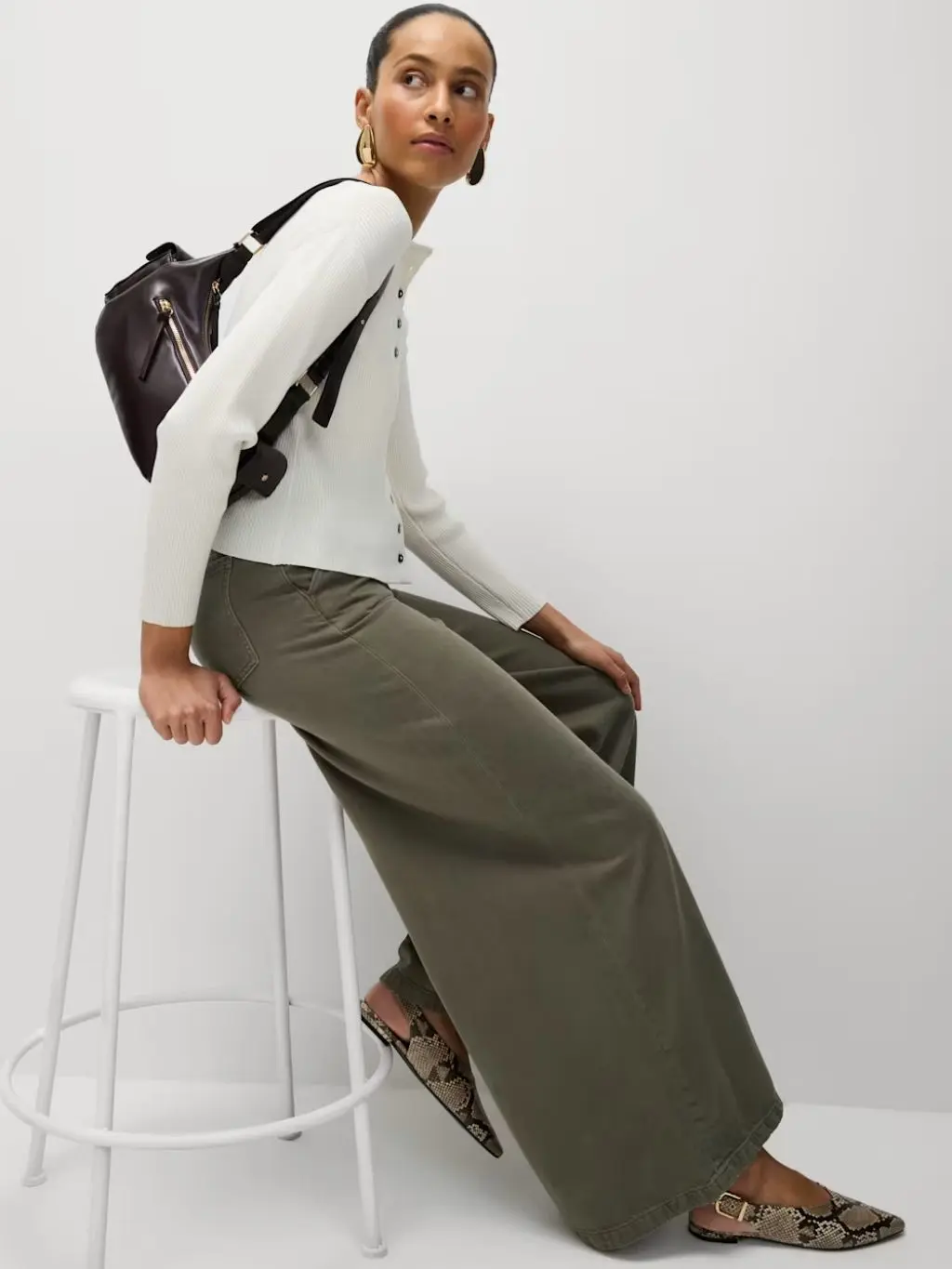 A woman sat on a stool wearing green wide leg trousers and a cream cardigan