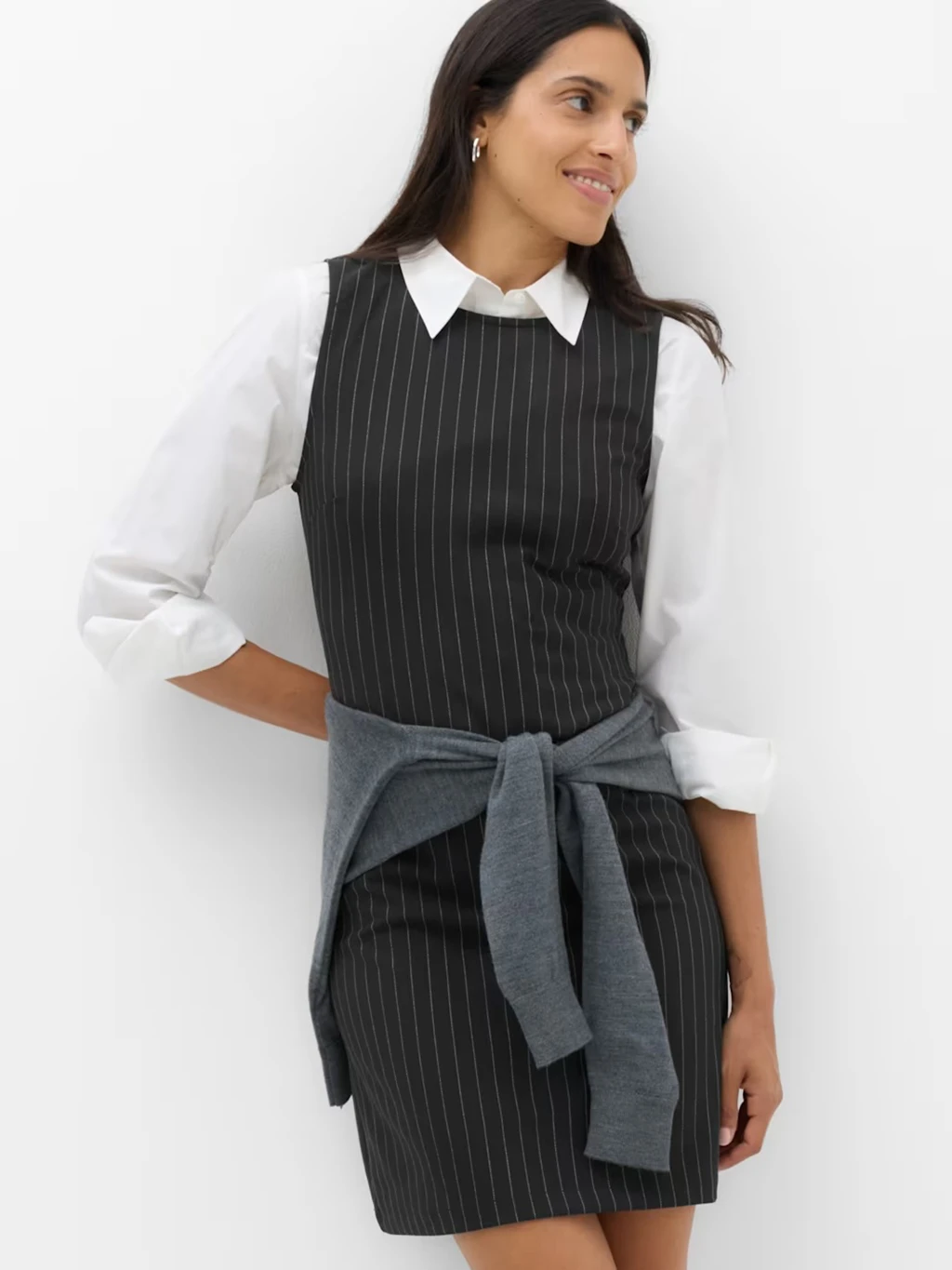 Women in a black pinstripe shift dress layered over a white collared shirt.