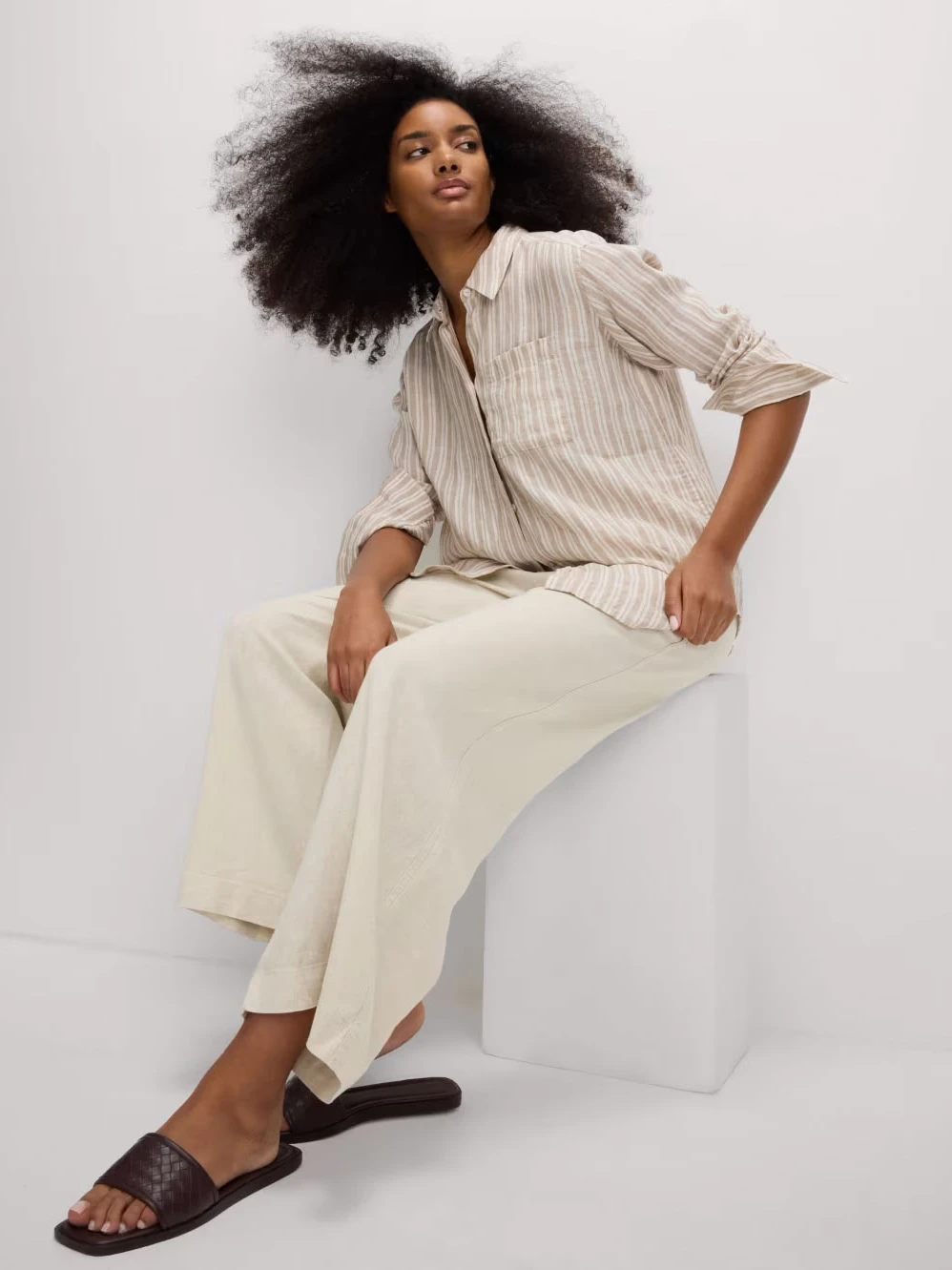 Woman wearing beige linen trousers with a striped shirt and sliders