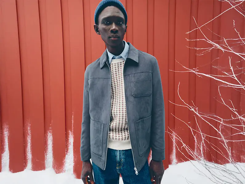 Man wearing a blue shirt, patterned jumper, blue jeans and a grey overshirt with a beanie