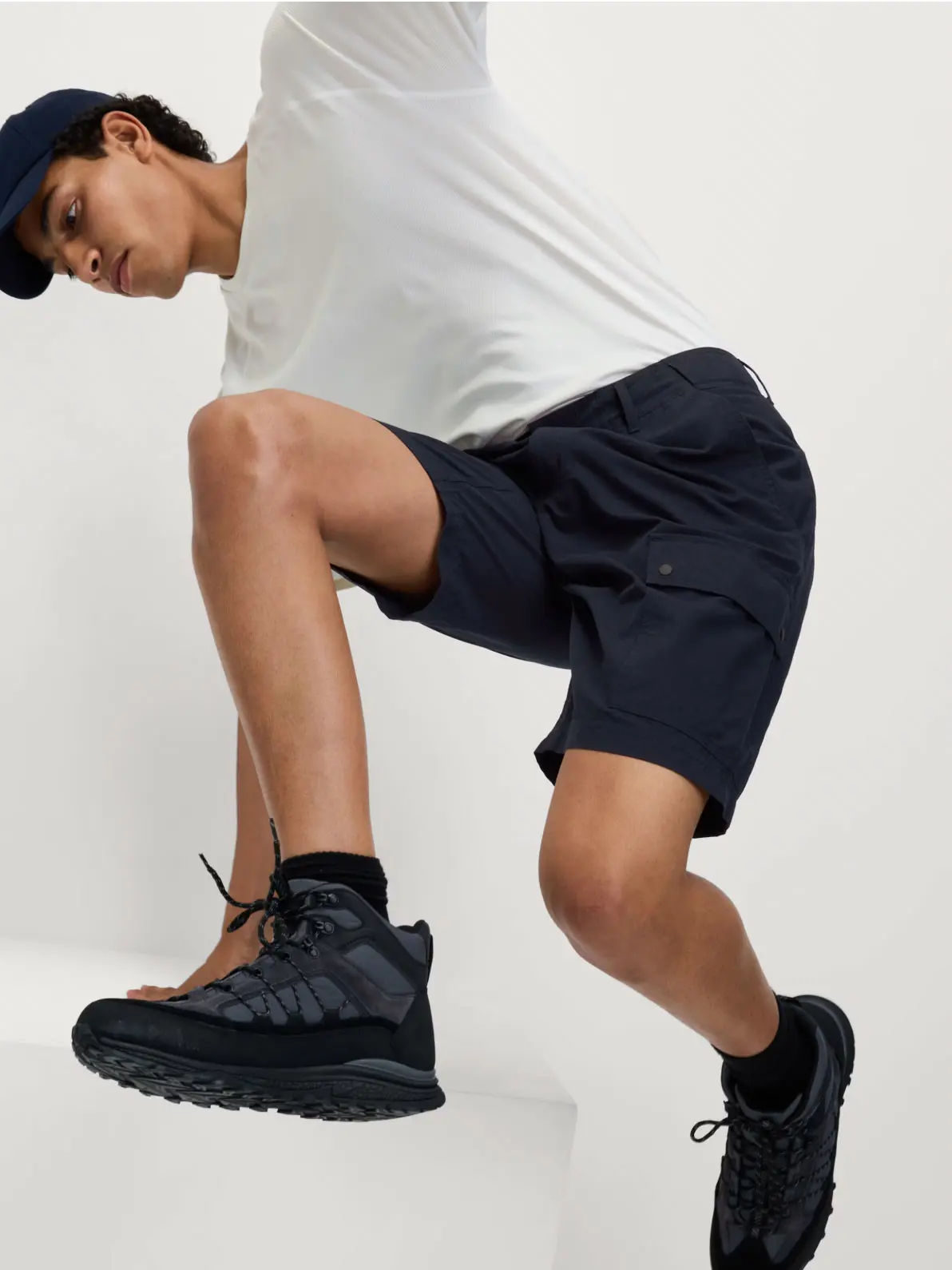 Man wearing white top, navy shorts, walking boots and navy cap