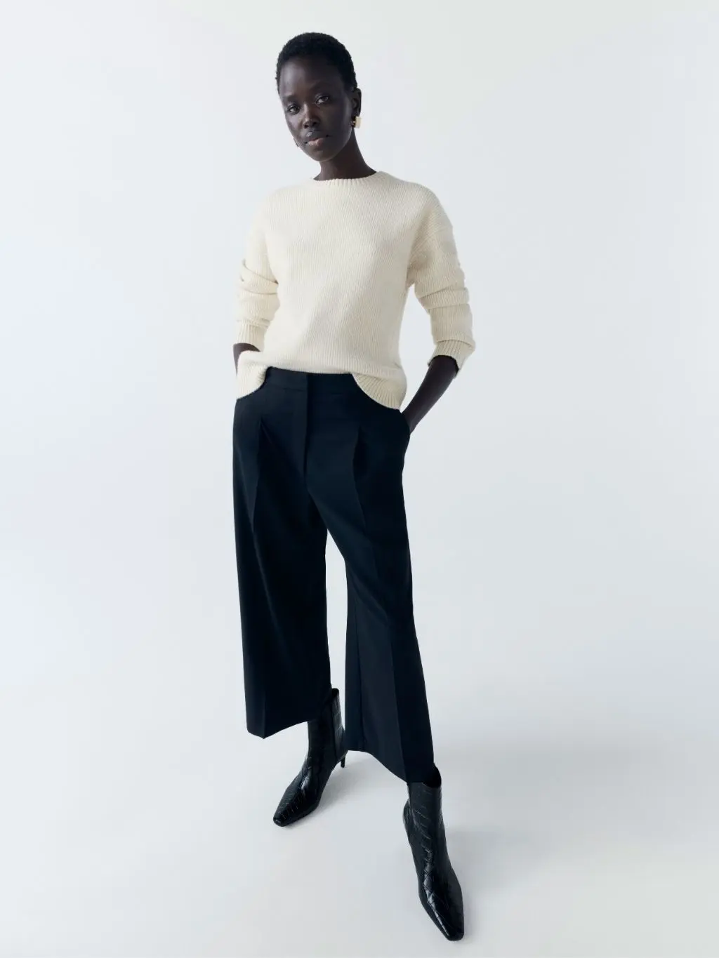 a woman wears a light top and cropped navy trousers with black ankle boots