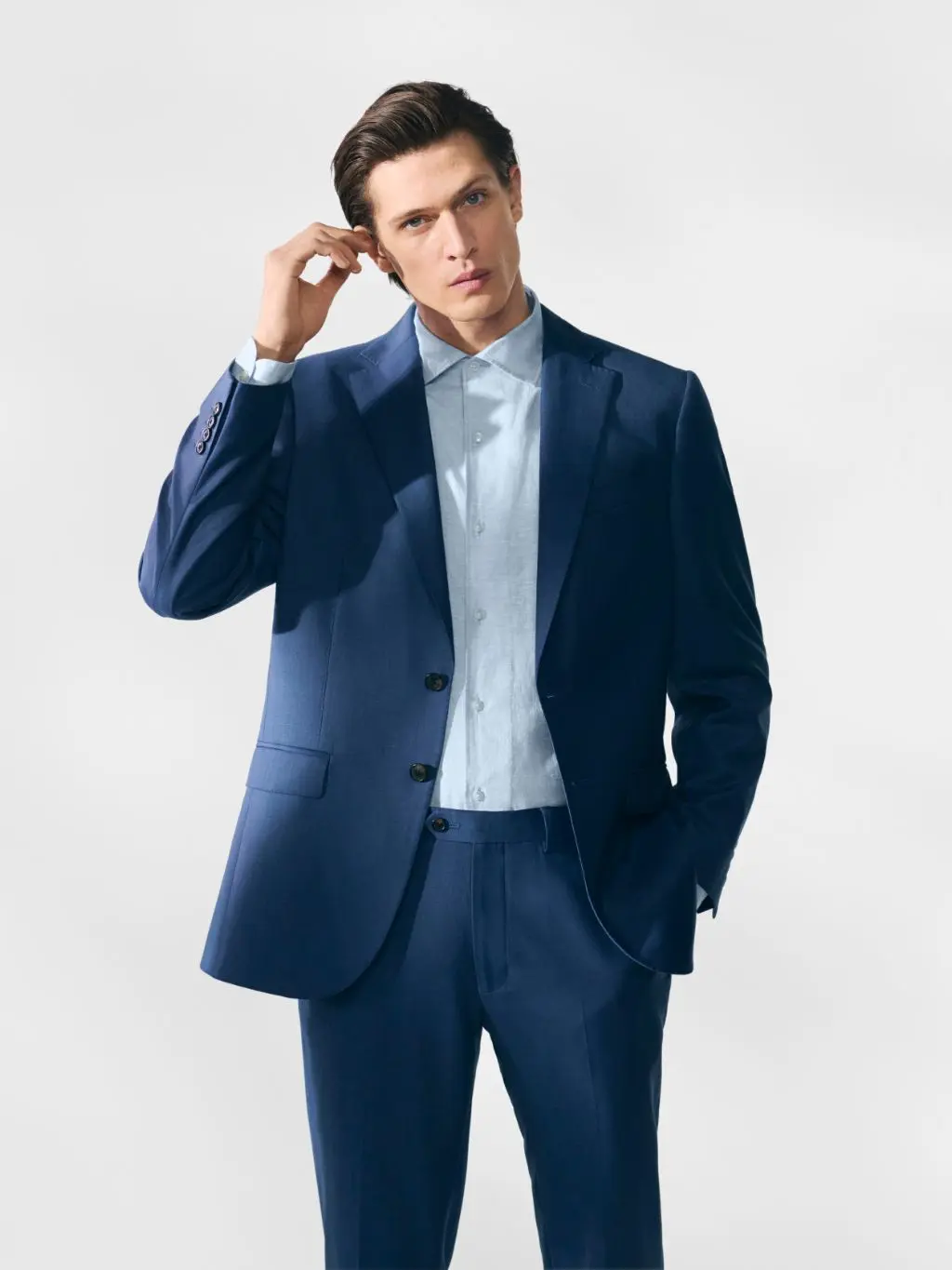 A man looking towards the camera, wearing a dark blue suit and lighter blue shirt