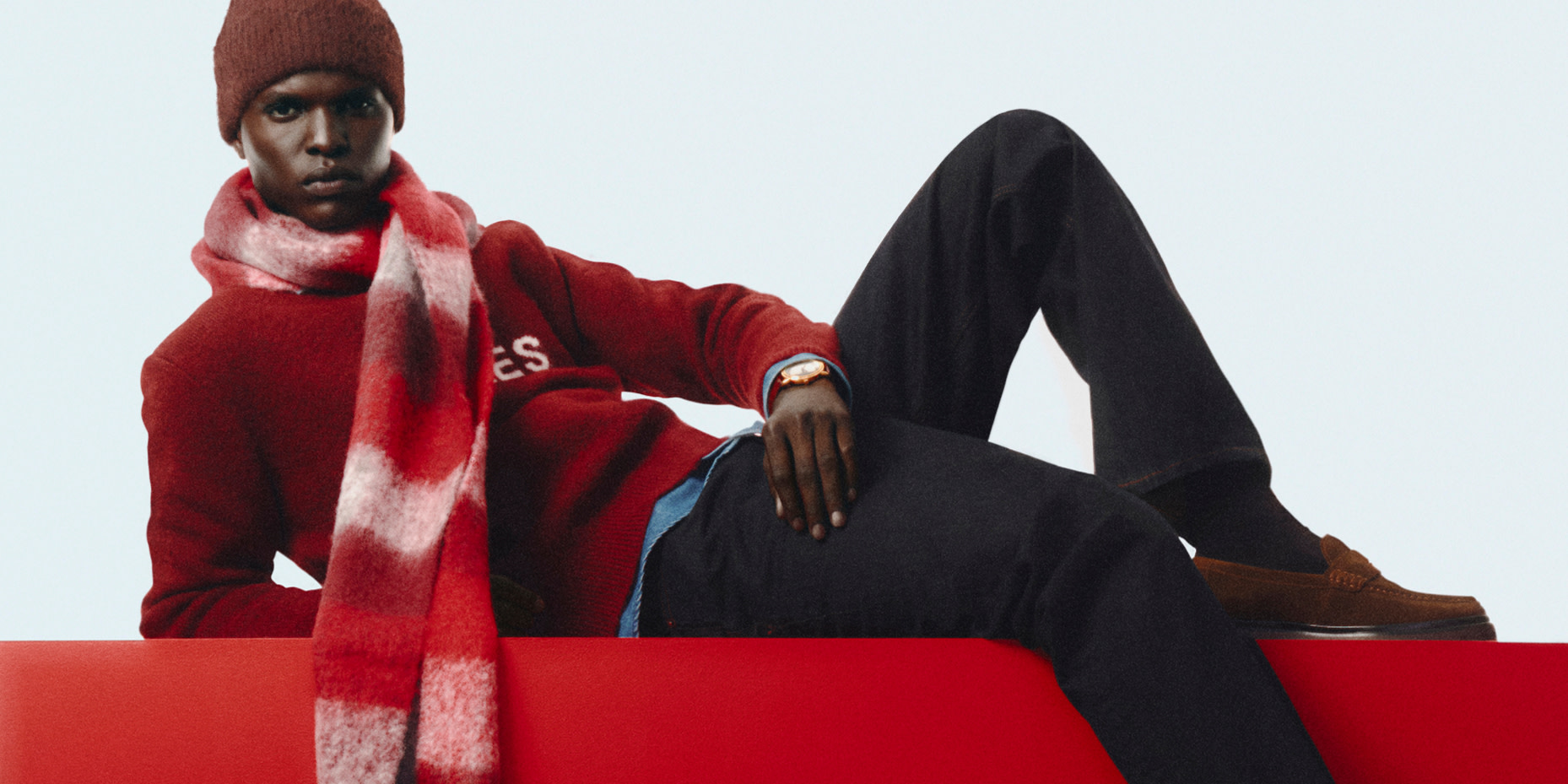Man in beanie, red jumper, black trousers and scarf