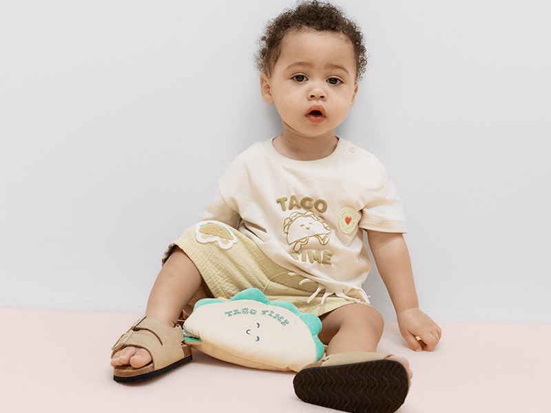 Baby wearing outfit with taco Tuesday graphic with a taco toy
