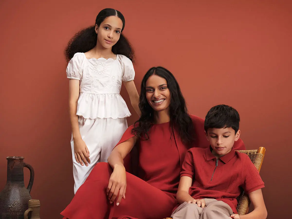Woman in red dress, young girl in white top and trousers, and young boy in red T-shirt and neutral trousers 