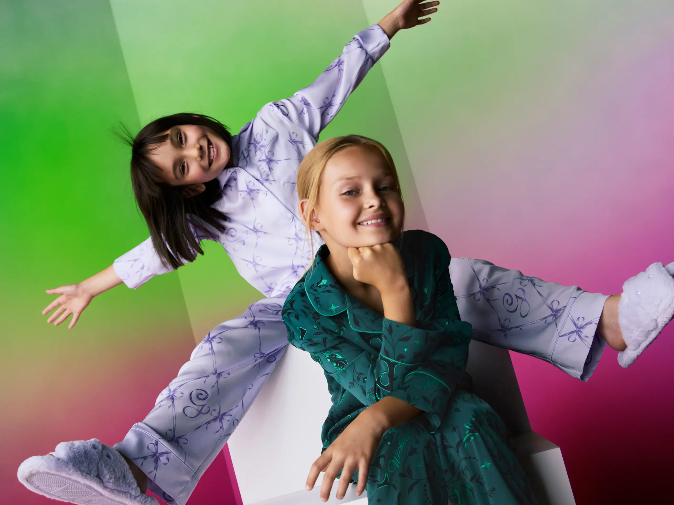 Image of two girls wearing Wicked themed pyjamas in lilac and emerald green 