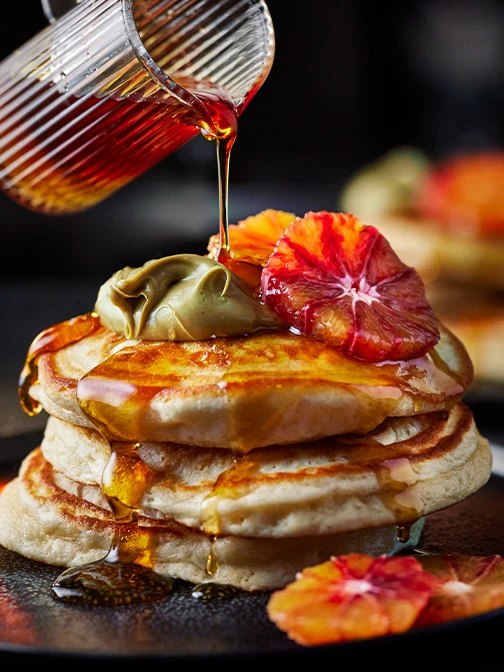 Pancakes with slices of blood orange, maple syrup, and pistachio creme