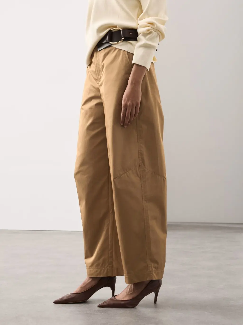 A close up of a woman wearing a waist belt over a jumper and trousers