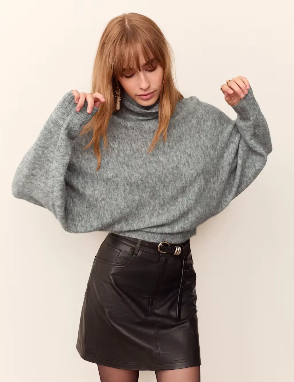 Model wearing a grey balloon sleeve jumper with a high roll neck, leather mini skirt and tights.