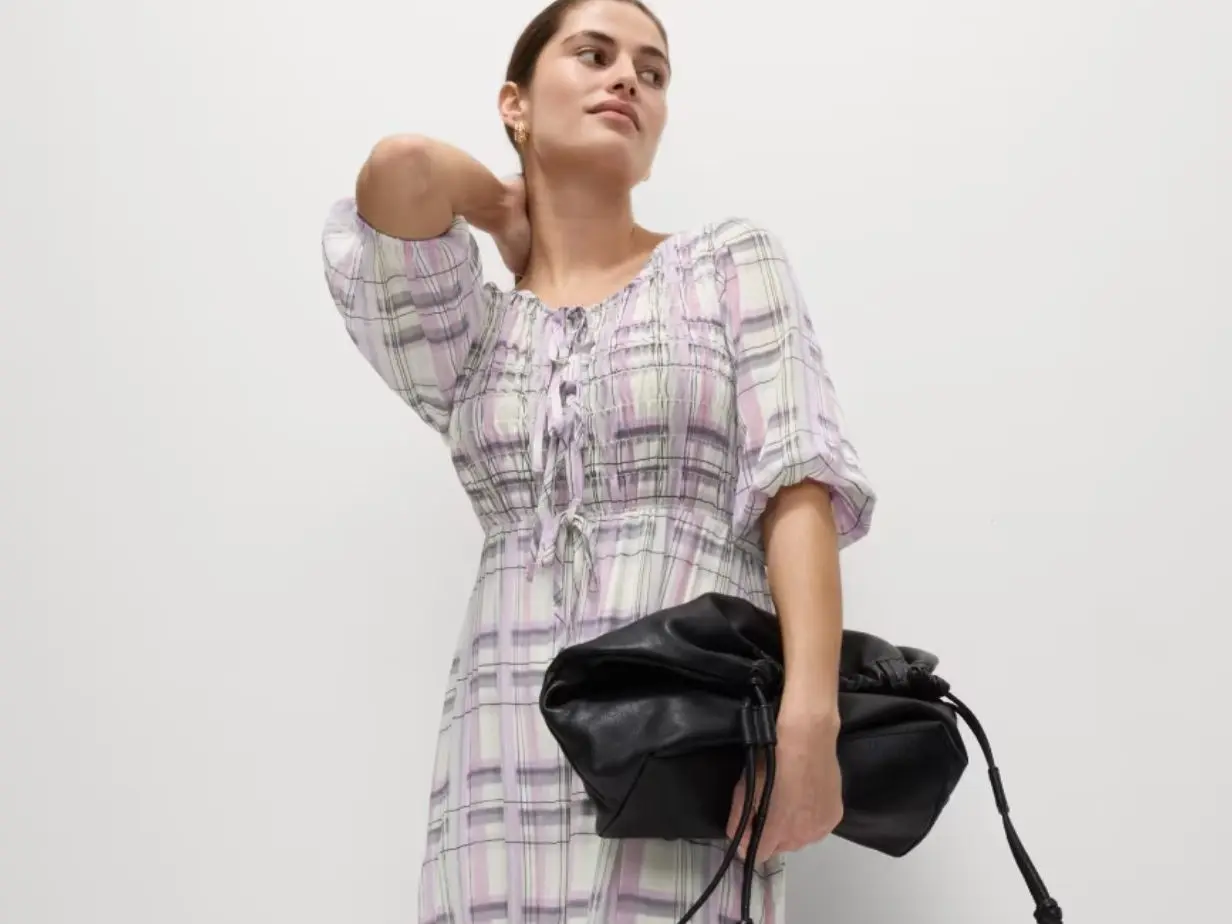 A woman wears a lilac check midi dress and carries a black handbag