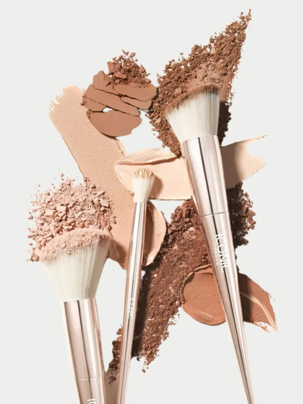 A range of makeup brushes shot against a light background, with smashed palettes of eyeshadow and powder around them
