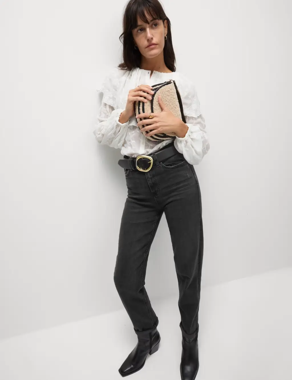 Woman wearing black straight-leg jeans with a white blouse, black belt, black cowboy boots and a woven cross-body bag.