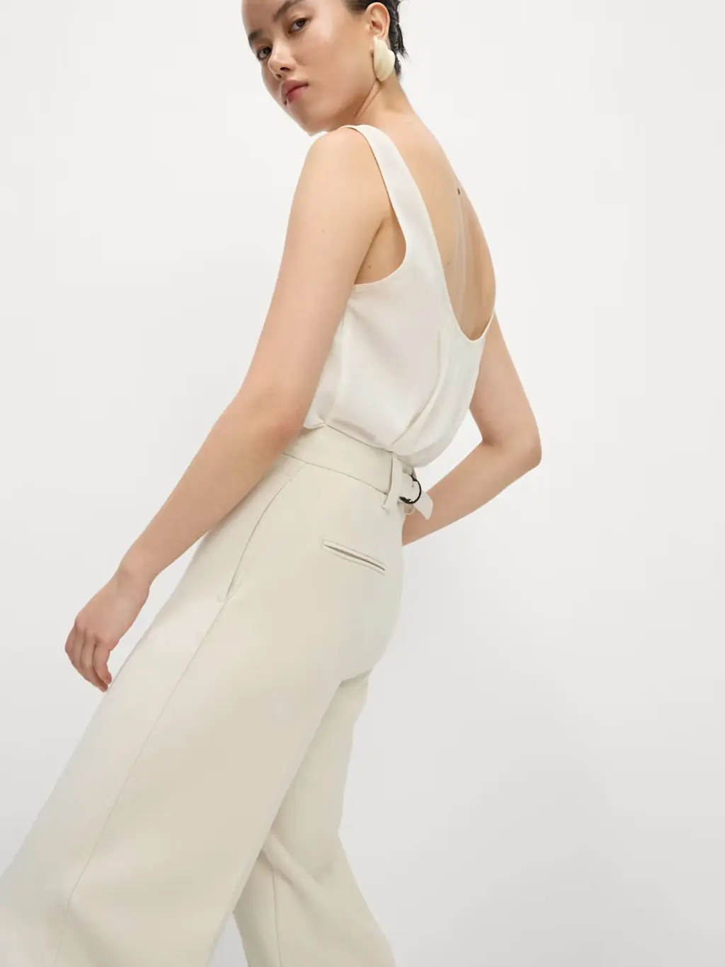 Woman wearing white crepe trousers with a white cami and statement earrings