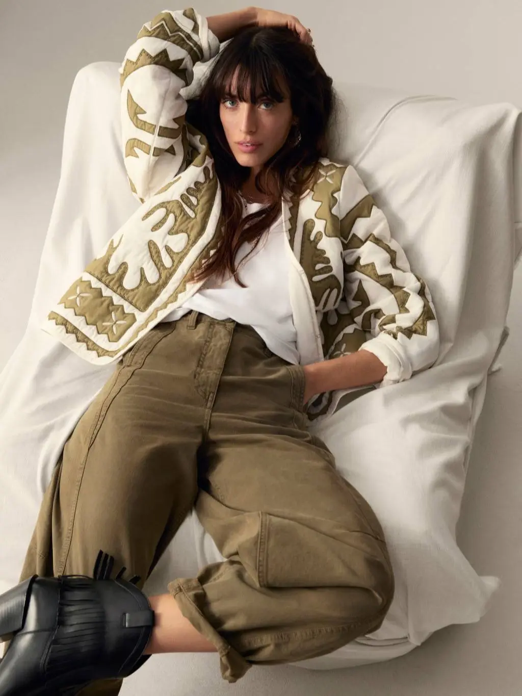 A woman lies back on a chair wearing a khaki and cream quilted jacket with cargo trousers and ankle boots
