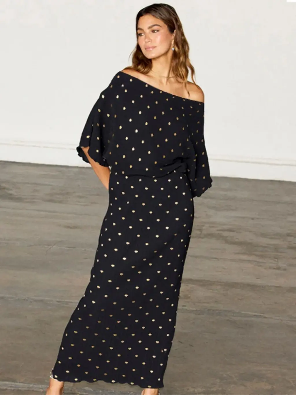 A woman wears a black and gold off-the-shoulder dress