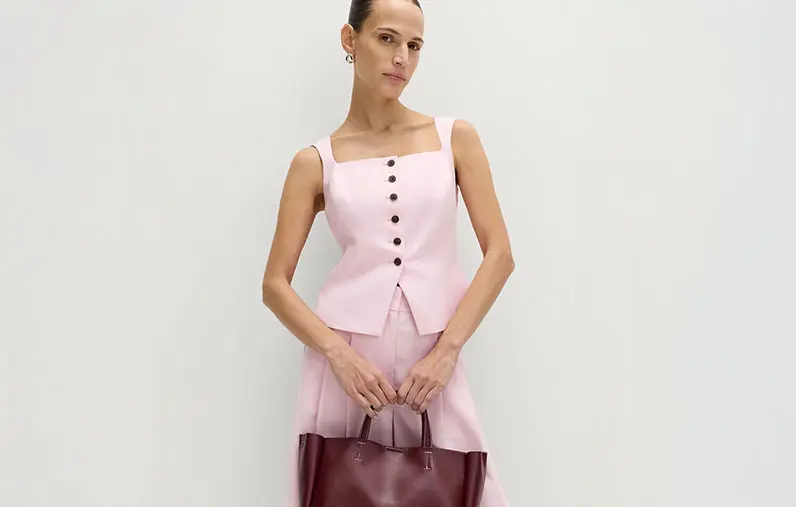 Woman wearing a pink waistcoat with matching trousers, silver jewellery and a burgundy bag