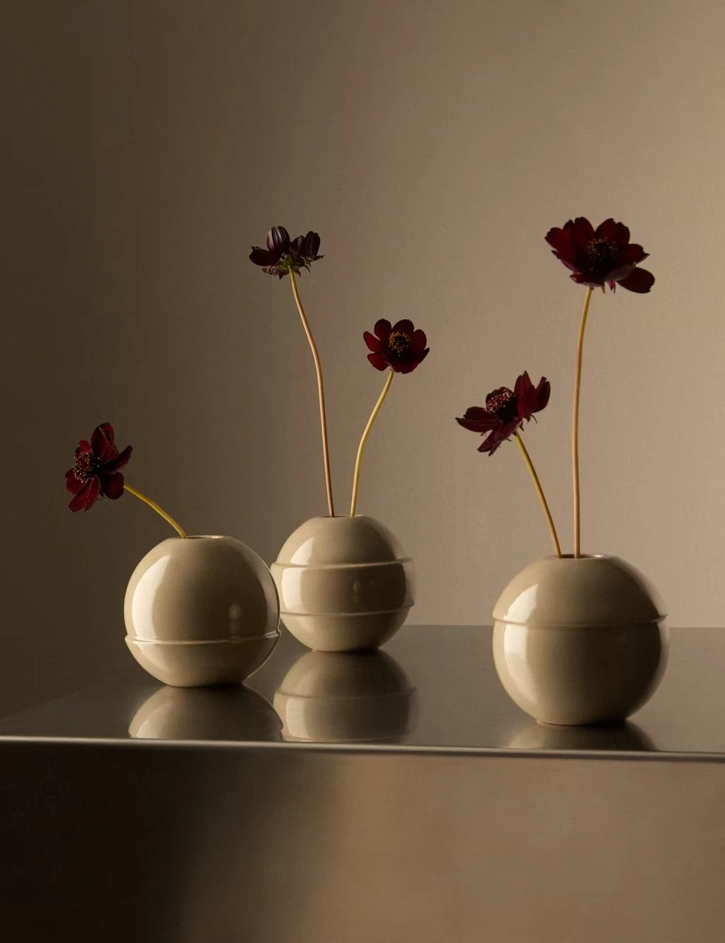 Trio of round bud vases in a soft neutral beige, filled with red stems.