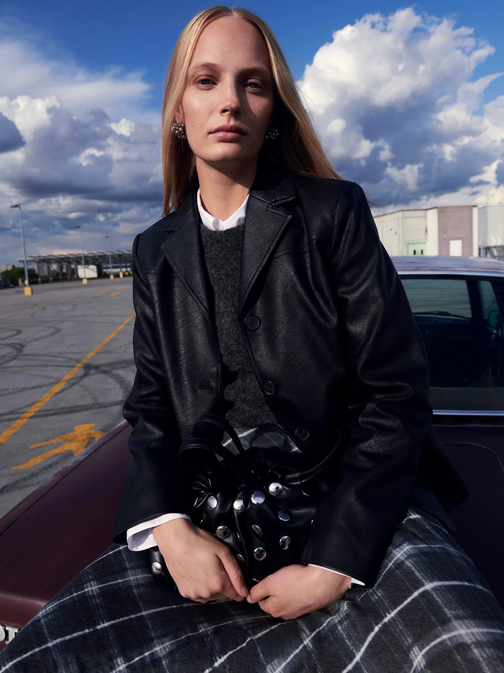 Woman wearing a black jacket over a dark grey checked dress with a black studded bag
