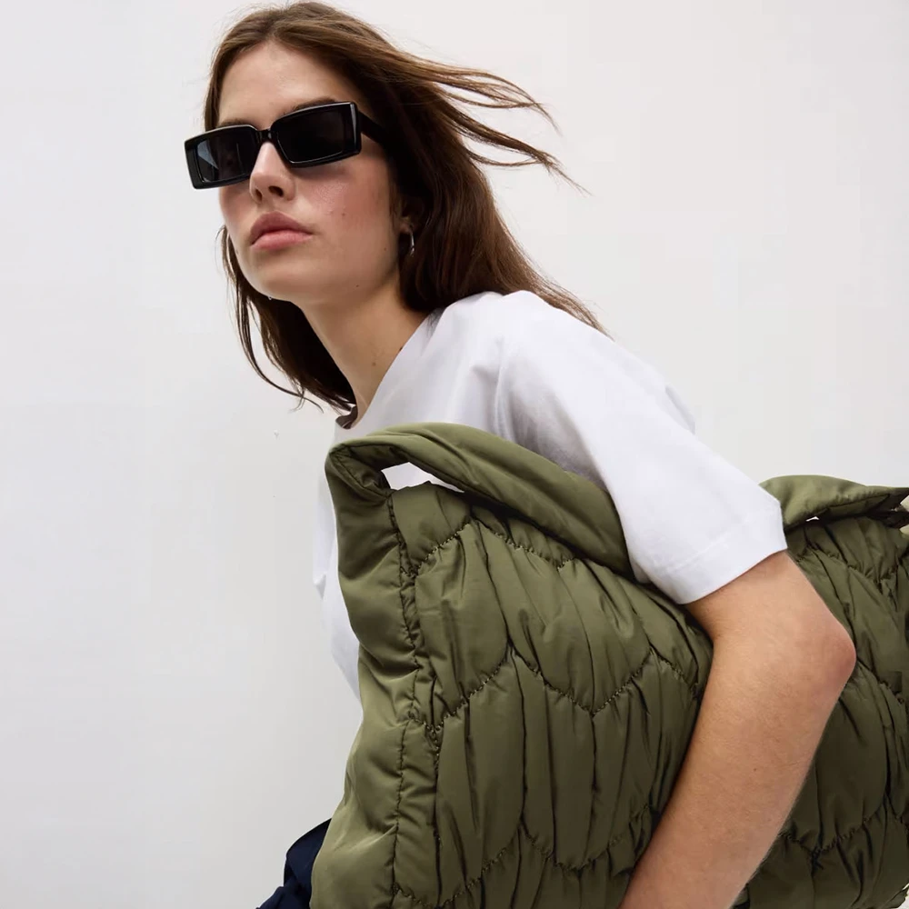 Woman wearing black sunglasses and white T-shirt holding khaki quilted bag