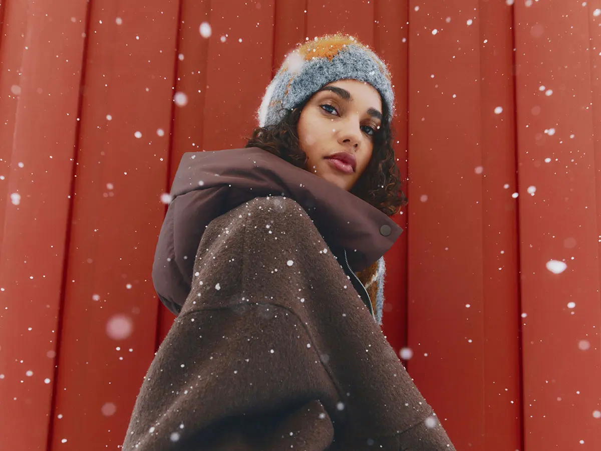 Woman wearing brown jacket and orange, grey and white beanie