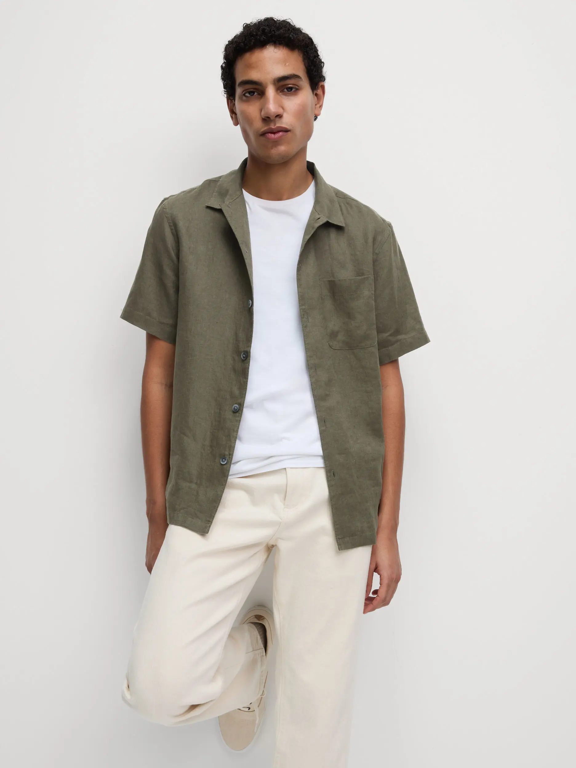 Man wearing a green linen shirt over a white T-shirt, with cream chinos