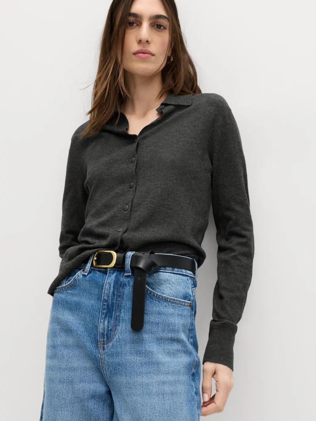 A woman wears high waisted jeans with a grey shirt and a black leather belt