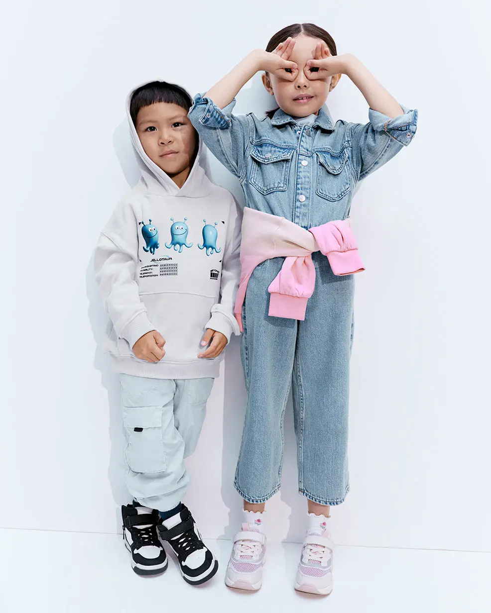 Girl wearing denim jumpsuit and boy wearing a hoodie and combat trousers at M&S