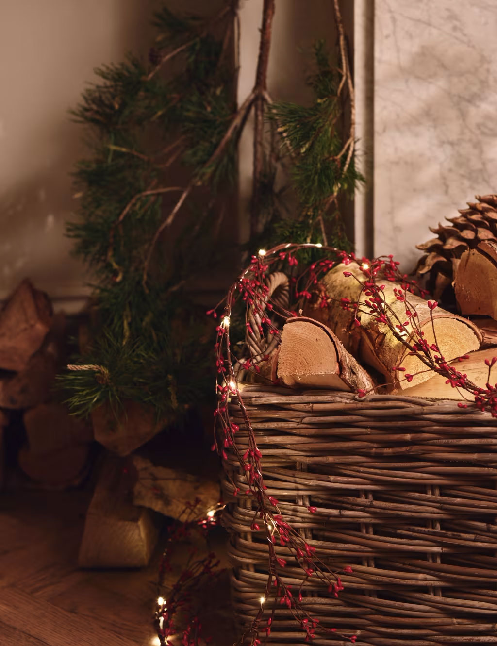 Berry garland fairy lights draped over a pile of logs by a fireplace