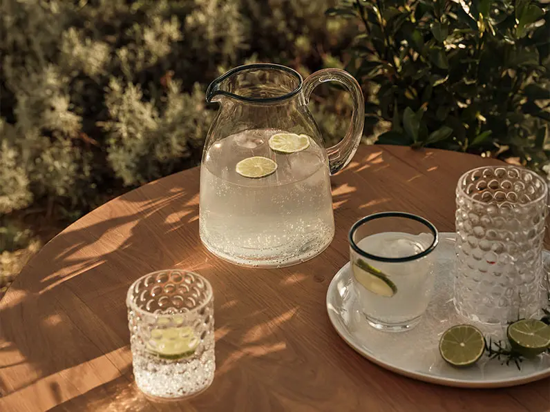 Jug and tumblers places on a outdoor table in dappled light