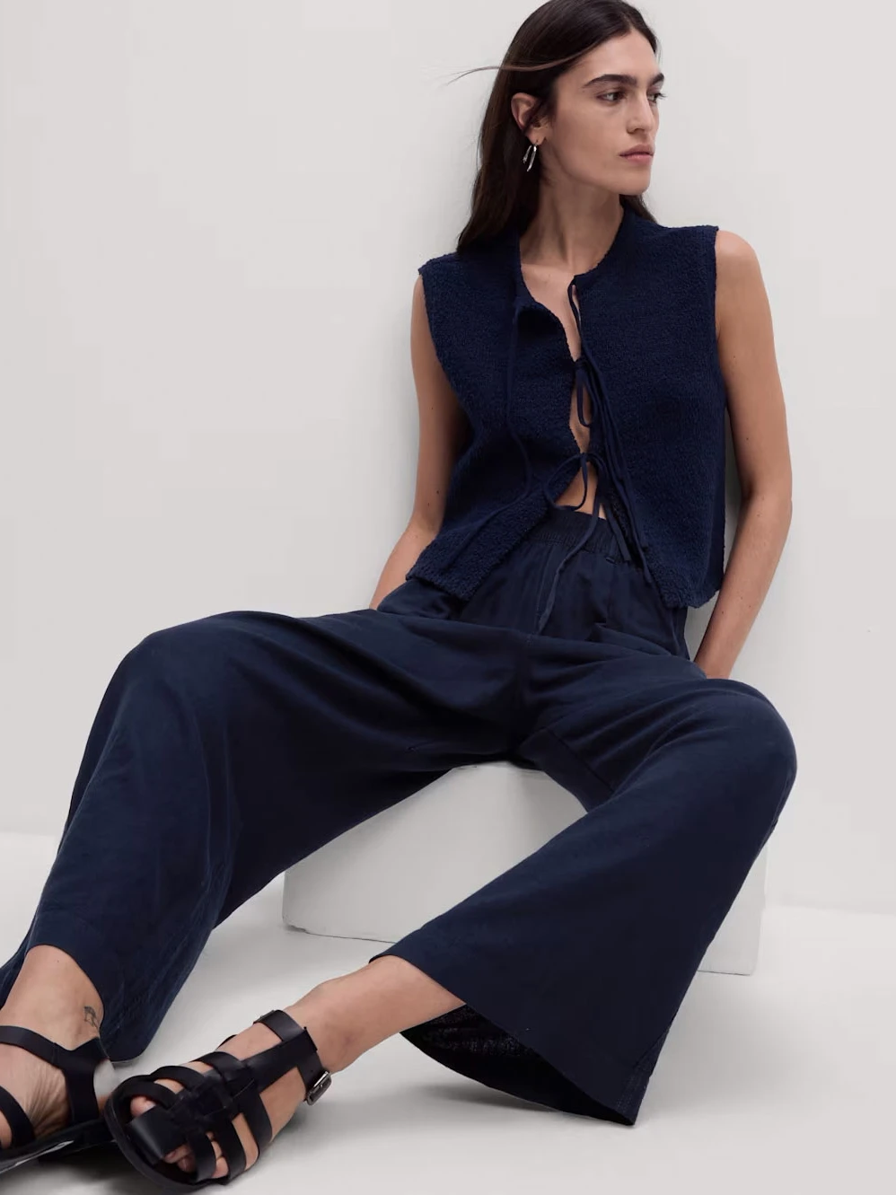 Woman wearing navy linen trousers with a tie-front top and sandals