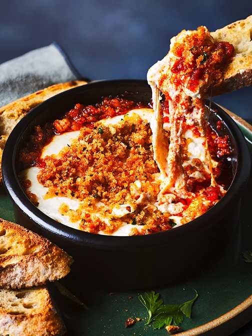 Slice of bread dipping into pot of hot burrata