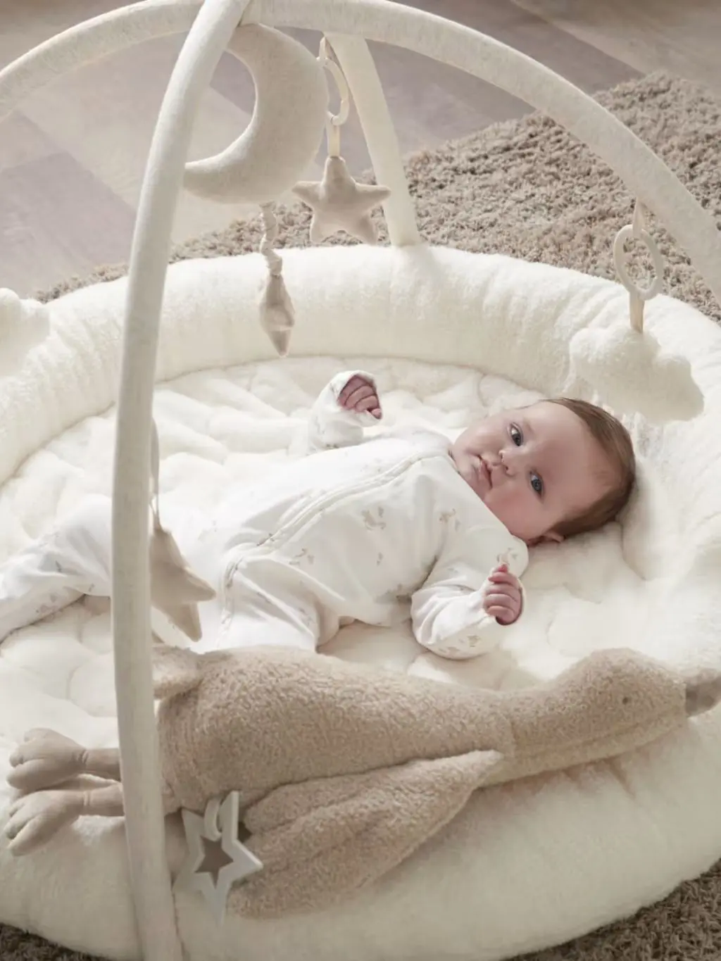A baby lies on a cream Mamas & Papas baby playmat