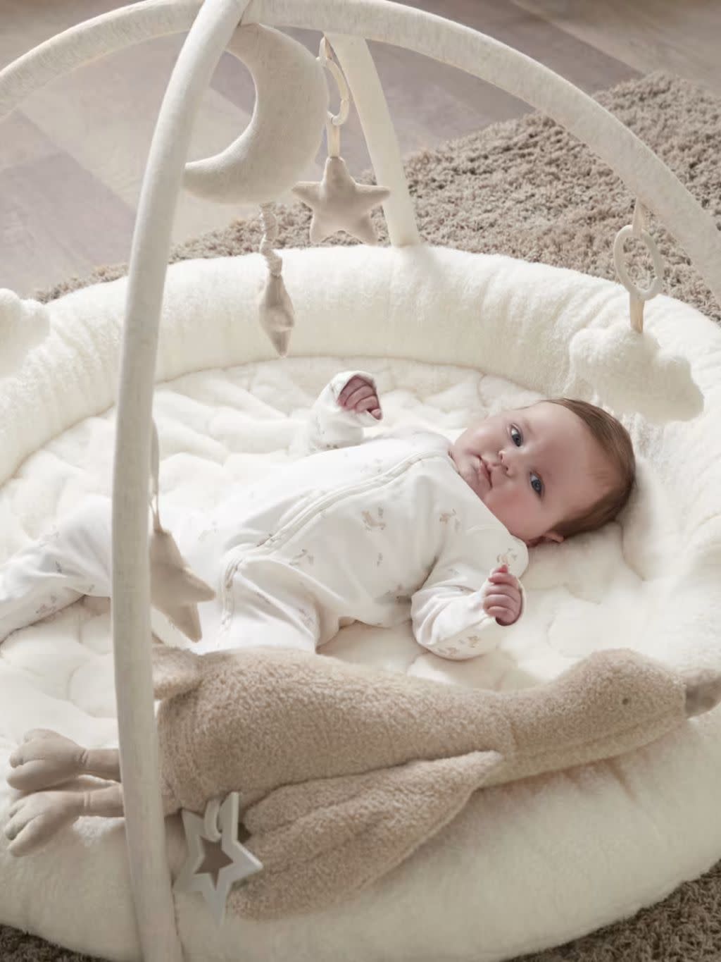 A baby lies on a cream Mamas & Papas baby playmat