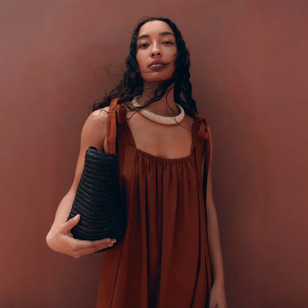 Woman wearing a rust-toned dress with a chunky beaded necklace and a black bag