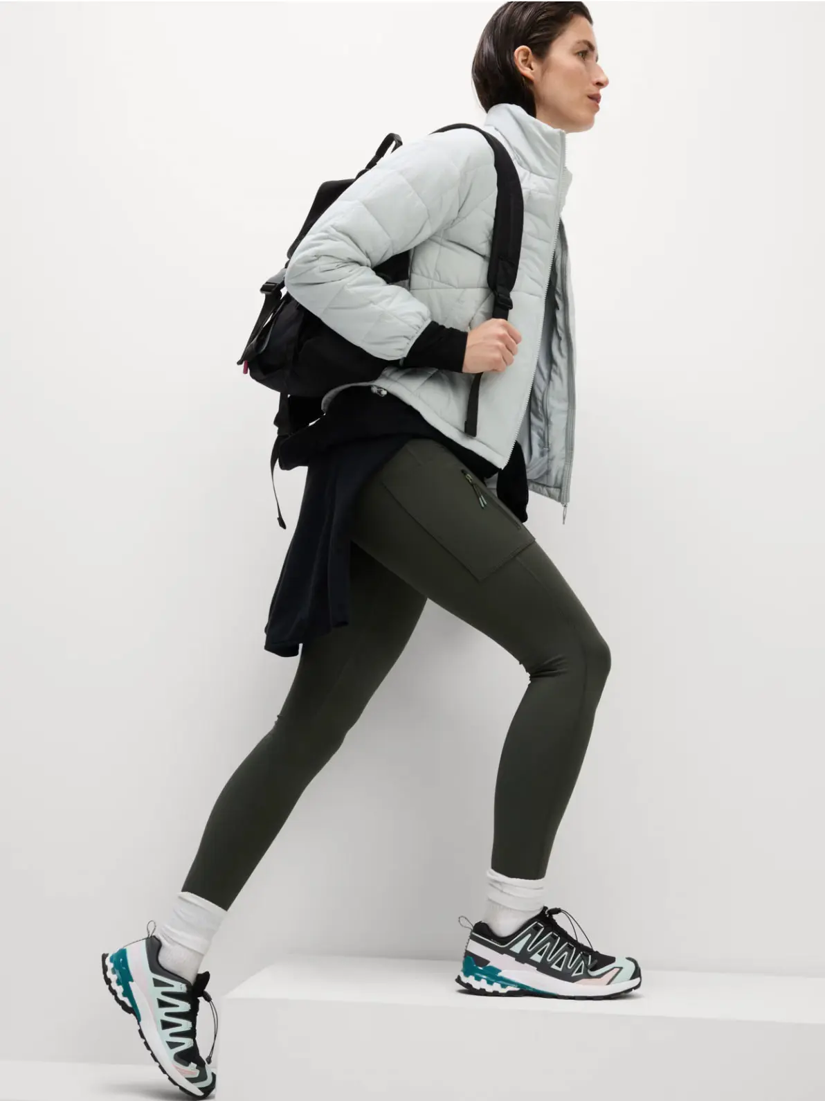 Woman wearing padded jacket, leggings, trainers and rucksack