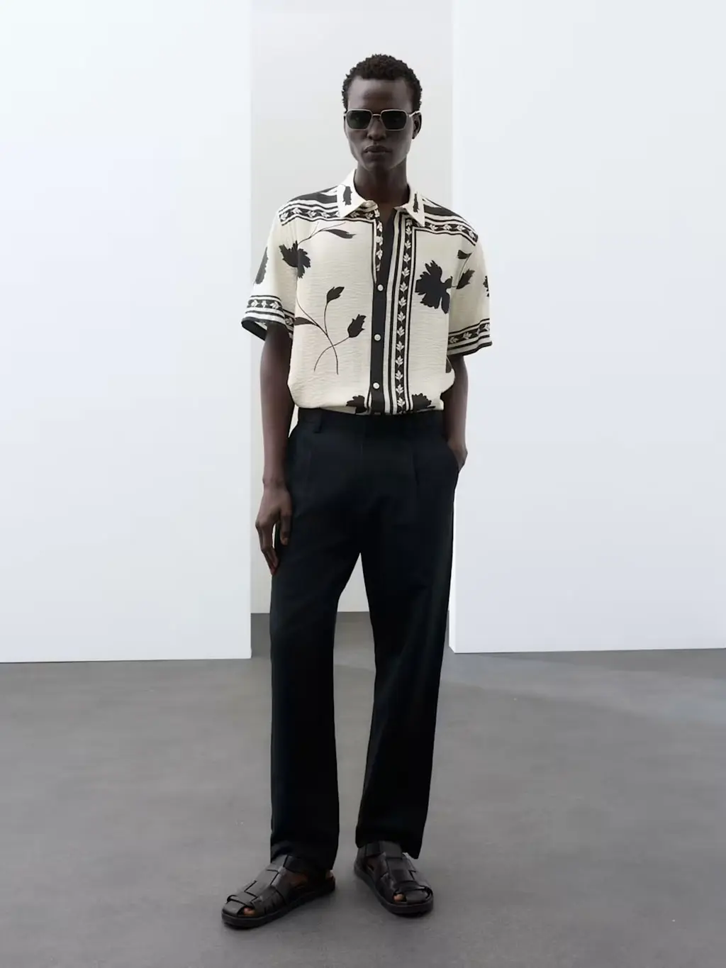 A man wearing a floral-printed shirt with black trousers and sandals