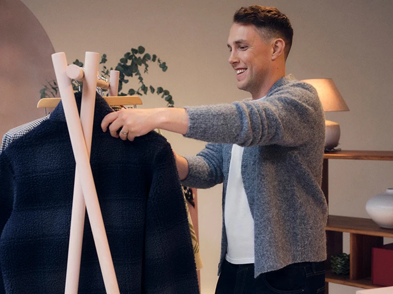 Chris Stark wearing a grey cardigan looking at a rail of clothing