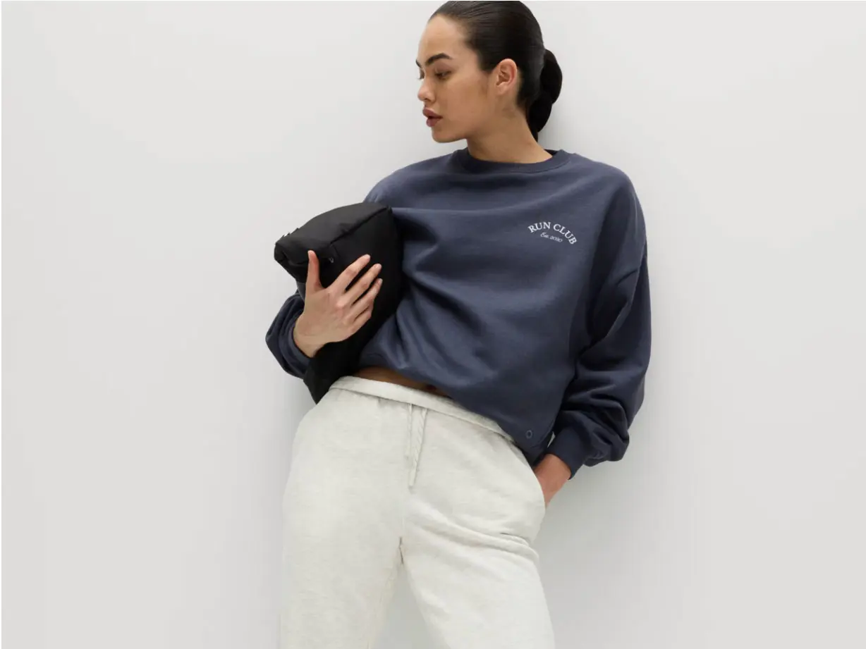 Woman wearing navy sweatshirt, joggers and holding black bag