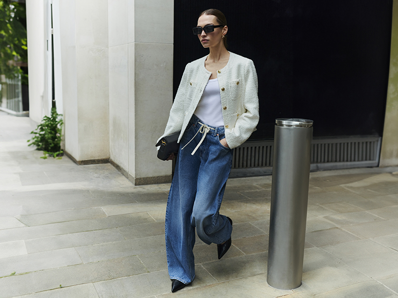 Woman wearing cream collarless jacket, white vest top and blue wide-leg 