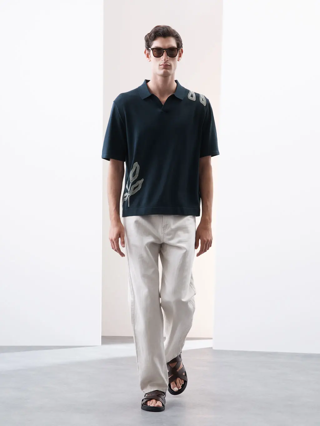 Man wearing a navy embroidered polo shirt and ecru jeans