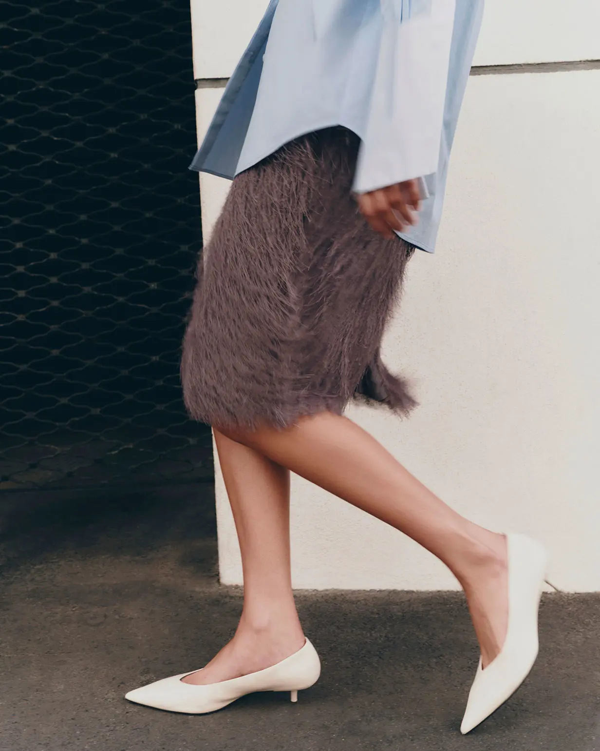 Woman wearing blue shirt with oversized contrast cuffs and brown fringed skirt