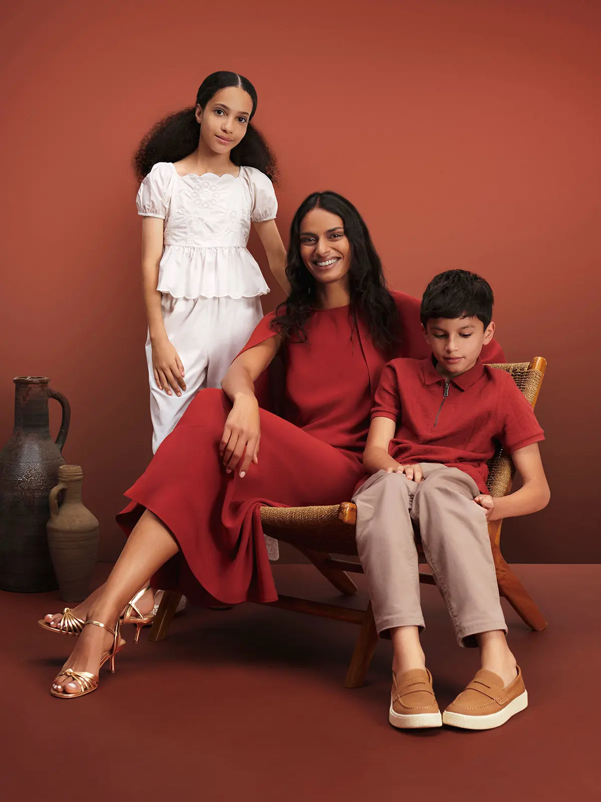 Woman in red dress and gold heels, young girl in white top and trousers, and young boy in red T-shirt and neutral trousers 