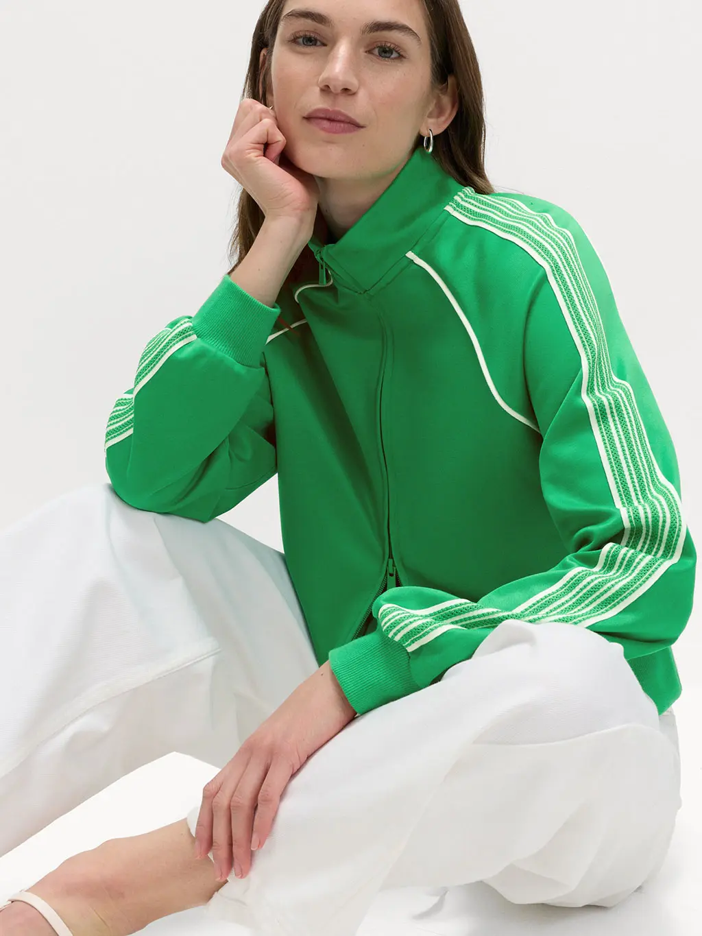 Woman wearing a green track jacket with white jeans