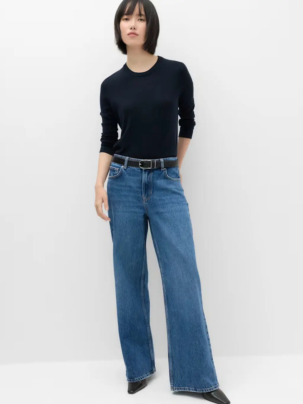 Woman wearing low-rise jeans with a navy top, black belt and black boots