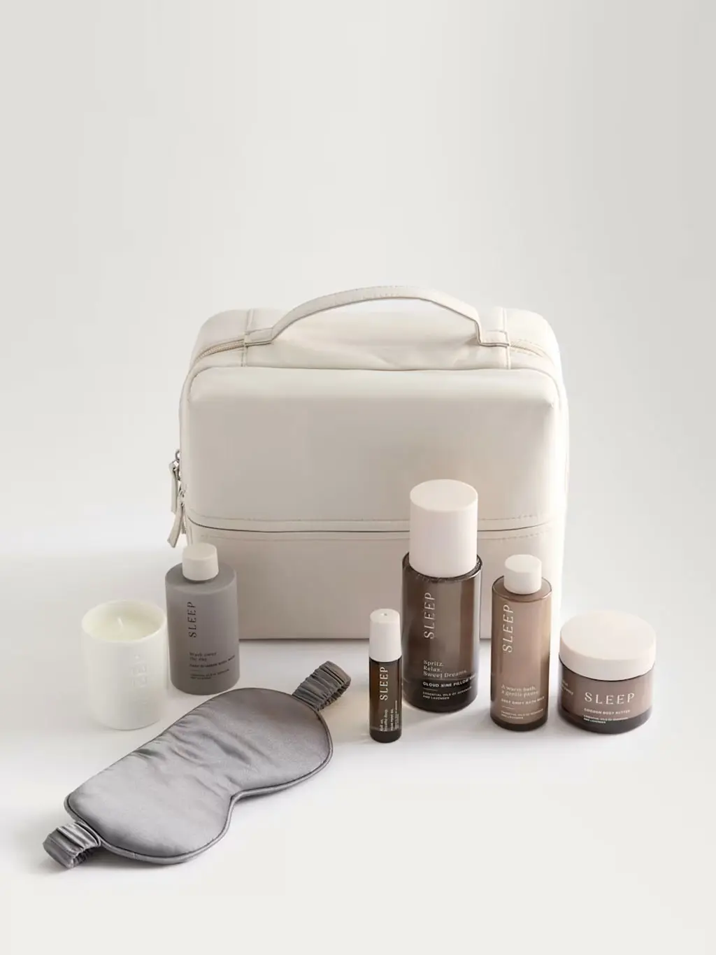 A cosmetic bag featuring a Deep Slumber body wash, Cocoon body butter and Deep Drift bath milk, alongside a Cloud Nine pillow mist, Sleep pulse point oil and fragranced votive candle.